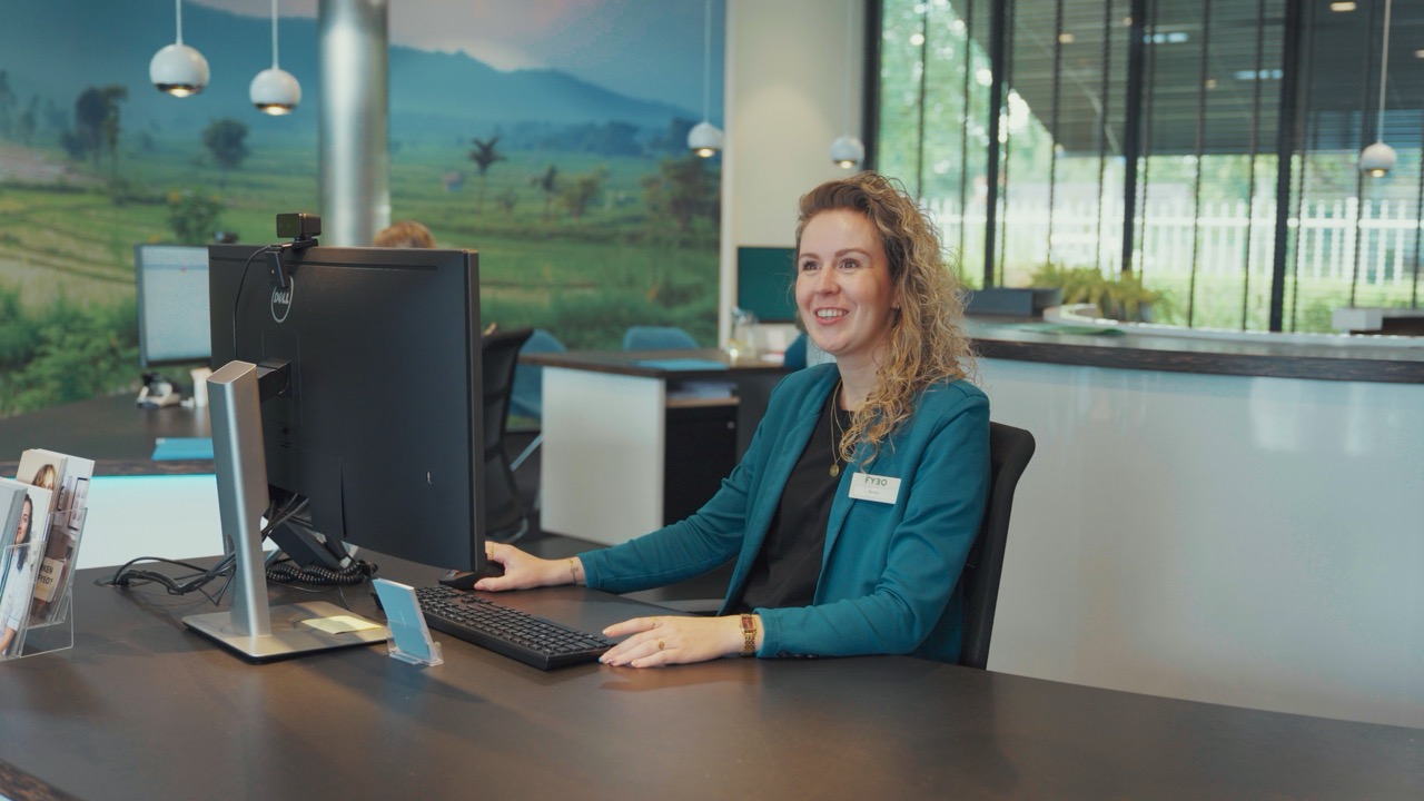 Medewerker lacht achter de computer aan de balie